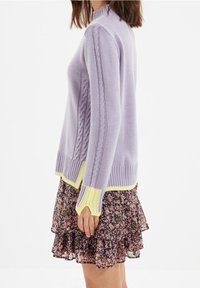 Maglione viola chiaro con dettagli a trecce, orlo e polsini a coste. Abbinato a una gonna nera a strati con motivi floreali.