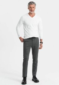 Weißes langärmliges V-Ausschnitt-Shirt kombiniert mit grauen Slim-Fit-Hosen und schwarzen Schnürschuhen, mit glatter Textur und maßgeschneidertem Design.