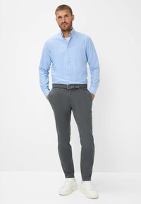 Chemise boutonnière bleu clair avec une poche, associée à un pantalon slim gris foncé et des baskets blanches. Tissu lisse avec une coupe soignée.