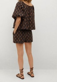 Sort blomster-mønstret top med korte ærmer og matchende shorts, med en afslappet pasform og letvægtsstof. Brune strop sandaler.