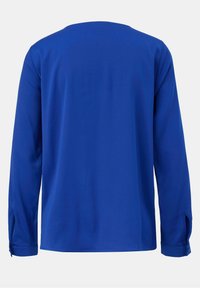 Chemise bleue à manches longues avec des poignets, en tissu lisse, et un col rond, présentée de dos sur un fond uni.