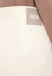 Tote bag i kremfarget faux skinn med en teksturert brun stoffdetalj. Har et grått merke med "MM" i hvite bokstaver.