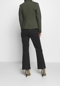 Olive green fitted blazer with long sleeves, paired with black flared pants and textured snakeskin ankle boots.