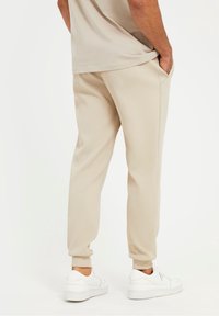 Beige Sweatpants aus weichem Stoff mit elastischen Bündchen und Seitentaschen, kombiniert mit weißen Turnschuhen. Schlichte, entspannte Passform.
