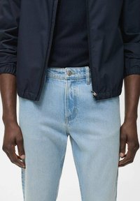 Chaqueta ligera color navy con puños elásticos, combinada con jeans de mezclilla azul claro con un corte clásico y detalles de costura visibles.