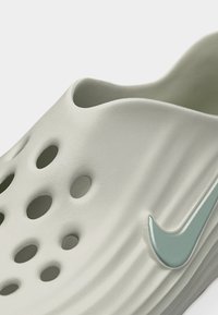 Lysegrå Nike slip-on sko med flere ventilationshuller og en lyseblå Nike swoosh på siden.