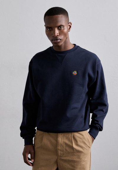 Marineblå bomulds sweatshirt med rund hals og ribbede manchetter, prydet med et lille flerfarvet broderet logo på brystet.