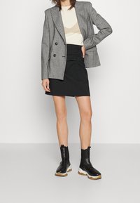 Šedý dvouřadý blazer s plochými klopami na béžovém topu, v kompletu s černou zřasenou sukní a černými kotníkovými botami s masivními bílými podrážkami.