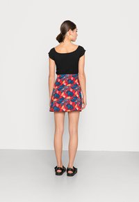Camiseta negra de rayas con mangas cortas, combinada con una falda roja de estampado floral con hojas azules, y sandalias negras.