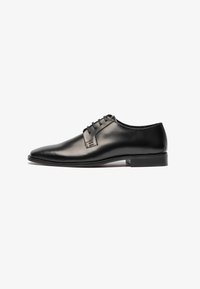 Zapato de vestir de cuero negro con un diseño elegante, punta afilada y cierre de cordones de cinco orificios. Textura suave y costuras mínimas. Suela de goma.