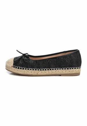 Zapato plano negro con parte superior de textil trenzado, puntera redondeada de yute, lazo decorativo y detalles cosidos a lo largo de la suela.