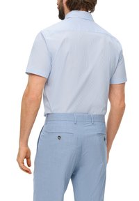 Camisa de manga corta de color azul claro con rayas verticales, vista trasera; combinada con pantalones azul claro que tienen bolsillos traseros y detalles de botones.