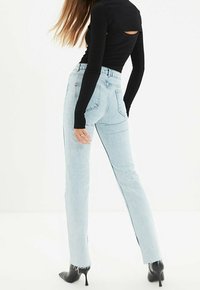 Jeans de mezclilla azul claro con pierna recta y dobladillo deshilachado, combinados con una blusa negra de manga larga que presenta un detalle cortado en la espalda.