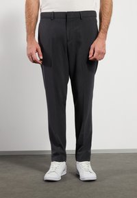 Grijze dresspants van een gladde stof, met een rechtlopende snit, plooien aan de voorkant en een tailleband met lussen. Gecombineerd met witte sneakers.