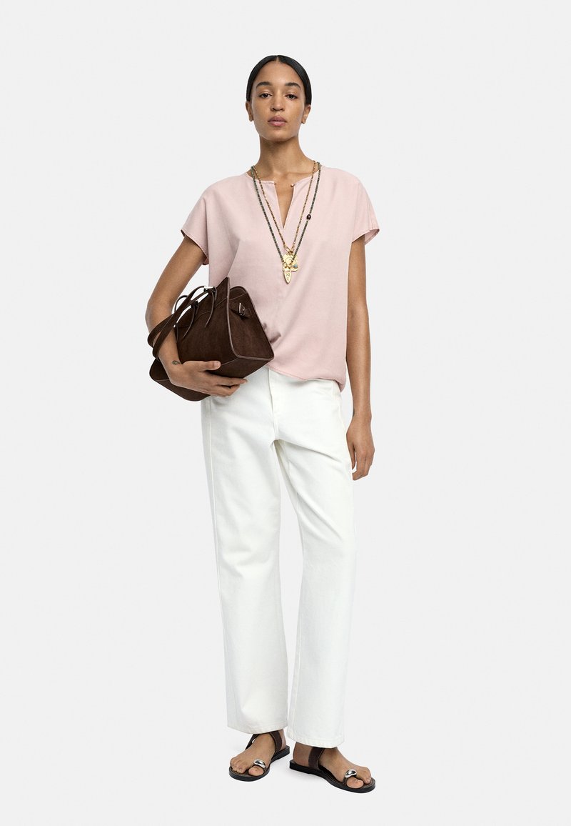 Jasnoróżowa bluzka z krótkim rękawem i dekoltem w kształcie litery V, w połączeniu z białymi spodniami o szerokich nogawkach. Brązowa torba na ramię i czarne sandały z metalicznymi akcentami.