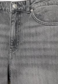 Gros plan sur la partie avant d’un jean denim gris présentant un bouton métallique, une fermeture éclair, des passants de ceinture et une poche avant.
