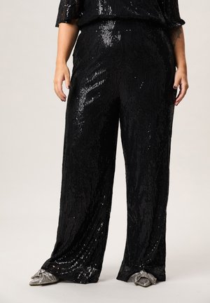 Zwarte, wijde broek met pailletten, gedragen met zilveren, puntige ballerina's met strik, getoond van halverwege de romp tot aan de voeten.