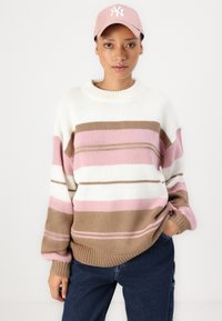 Knit sweater with a round neck, featuring horizontal stripes in pink, white, and brown. Paired with dark blue jeans and a light pink cap.