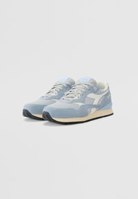 Light blue sneakers featuring a mix of smooth and textured materials, with mesh panels, padded collar, and black rubber sole.