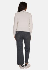 Maglione bianco a coste, jeans grigi a vita alta e scarpe sportive bianche con dettagli neri. Il maglione presenta un piccolo dettaglio sul retro.