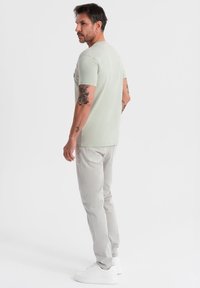Camiseta de algodón verde claro con mangas cortas y cuello redondo, combinada con jeans gris claro y zapatillas blancas. Diseño sencillo, sin patrones visibles.