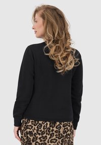 Felpa nera con un design semplice, polsini e orlo a coste. Abbinata a una gonna a pieghe con stampa leopardata. Capelli acconciati in morbidi ricci.