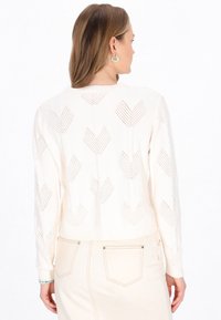 Maglione corto color crema con un motivo a maglia testurizzato e design a zigzag. L'orlo e i polsini a coste aggiungono struttura.