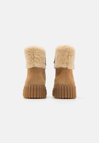 Botas de tobillo de ante marrón con un cuello de piel sintética, suela de goma marrón con textura, que presentan un zipper en el lateral y un acabado suave y texturizado.