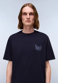 Marineblaue Baumwoll-T-Shirt mit rundem Halsausschnitt und kurzen Ärmeln, ausgestattet mit einem dezenten grauen Logo auf der linken Brustseite.