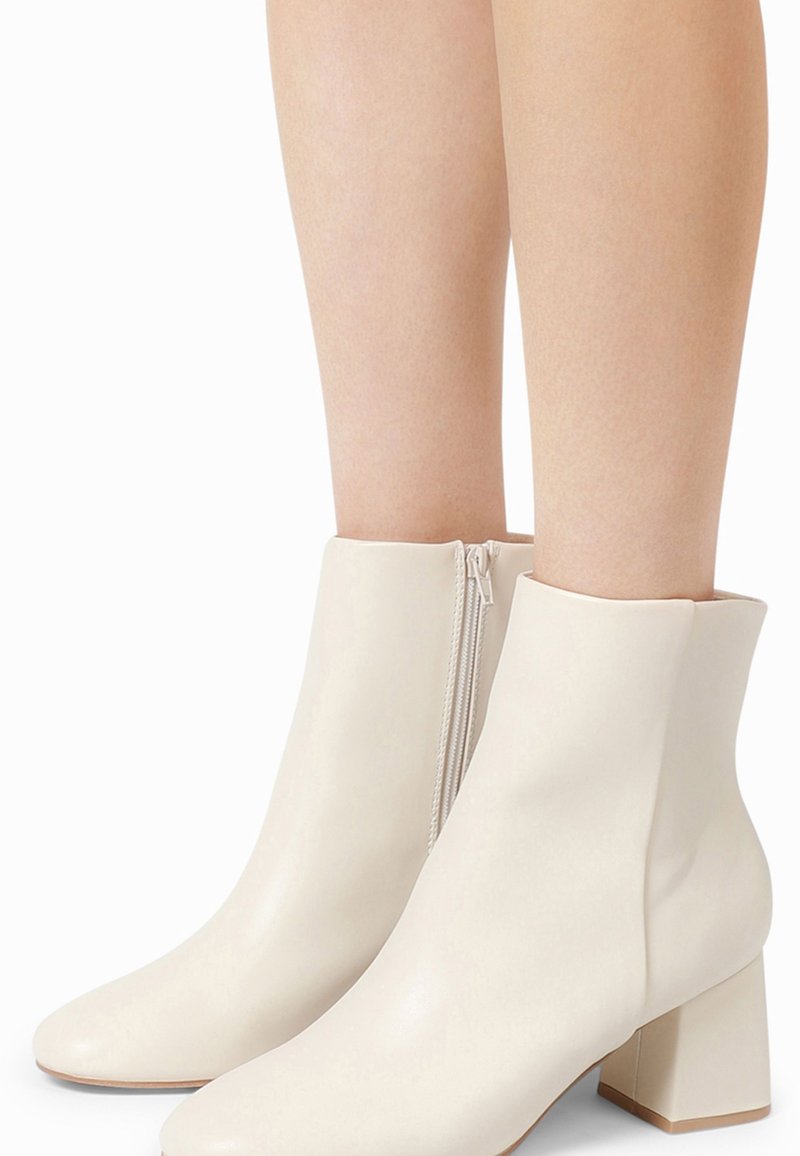 Bottines blanches avec une texture en cuir lisse, bout arrondi, talon moyen en bloc et détail de fermeture éclair sur le côté.