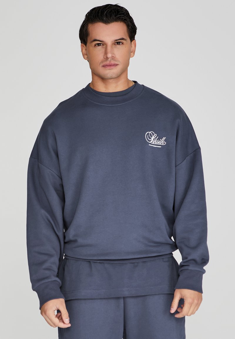 Marineblauwe sweatshirt met een ronde halslijn, verlaagde schouders en een klein wit logo op de linkerborst. Gladde textuur, relaxte pasvorm.