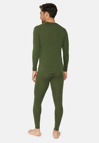 Grön långärmad thermotröja och matchande leggings i strukturell tyg, åtsittande design och minimala sömmar, sedd bakifrån.