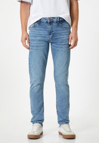 Vaqueros de un azul claro con un diseño ajustado, fabricados en denim, con patrones desgastados y acentos de costura. Combinados con zapatillas blancas.