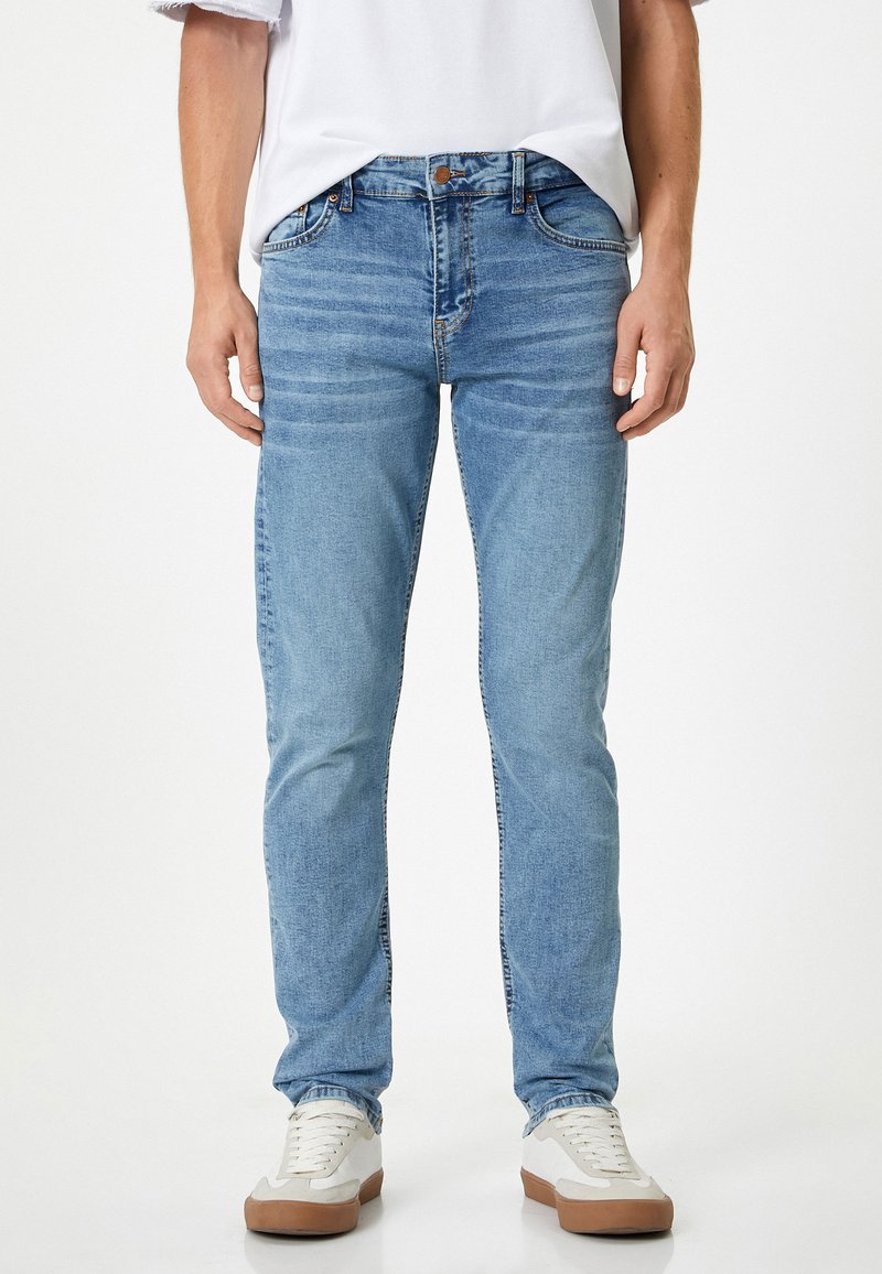 Vaqueros de un azul claro con un diseño ajustado, fabricados en denim, con patrones desgastados y acentos de costura. Combinados con zapatillas blancas.