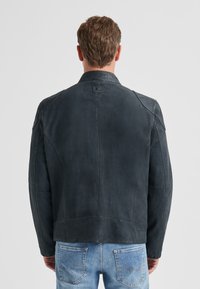 Dunkelgraue Lederjacke mit strukturiertem Design. Verfügt über einen kleinen Kragen, lange Ärmel und sichtbare Nähte. Getragen über hellblauem Denim.