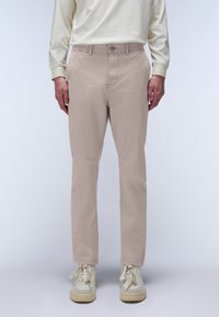 Chino beige slim fit realizzati in un tessuto misto cotone, con una texture liscia, cinque tasche e chiusura a un bottone. Abbinati a sneaker chiare.