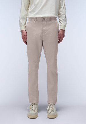 Chinos beige de corte slim, hechos de una mezcla de algodón, con una textura suave, cinco bolsillos y un cierre de botón único. Combinados con zapatillas ligeras.
