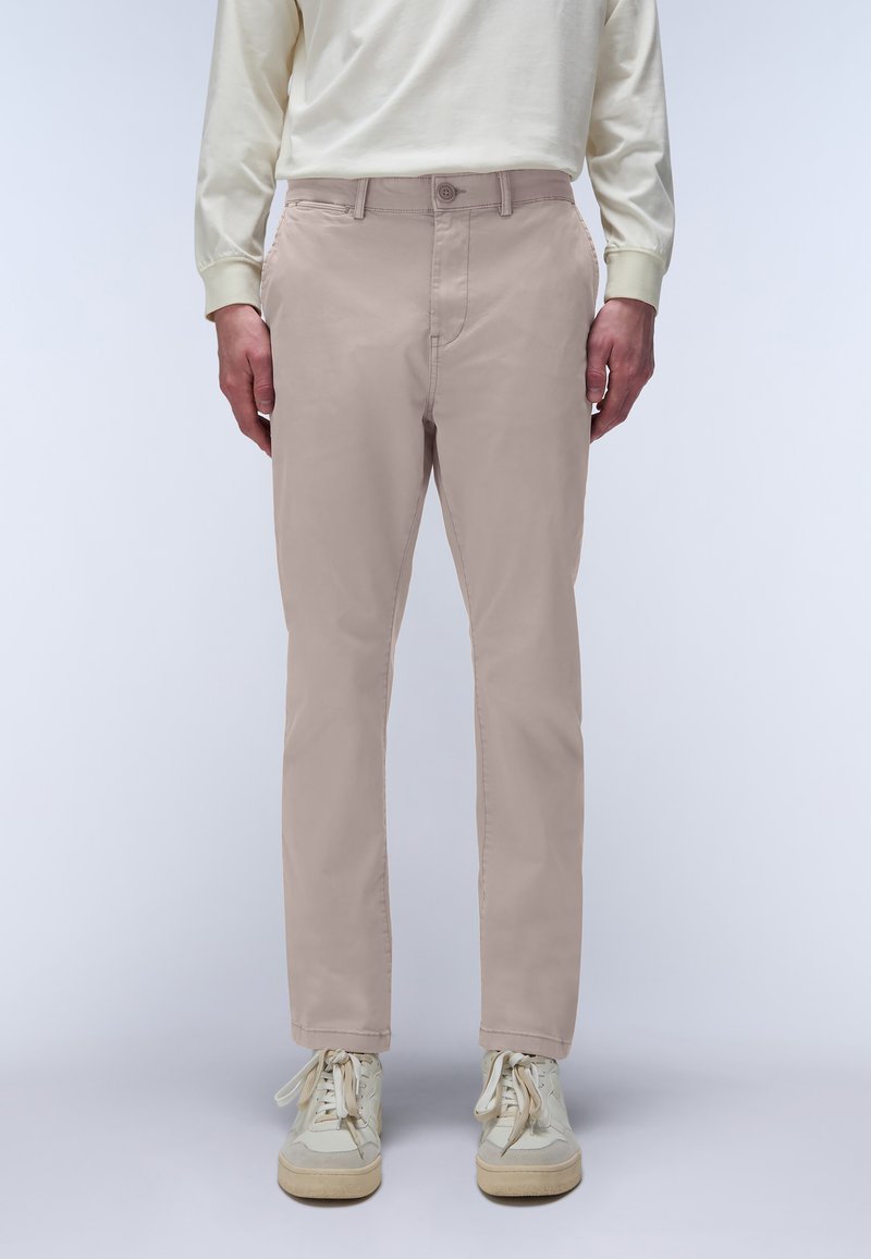 Chino beige slim fit realizzati in un tessuto misto cotone, con una texture liscia, cinque tasche e chiusura a un bottone. Abbinati a sneaker chiare.