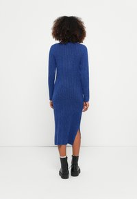 Blue ribbed dress with long sleeves, knee-length, features a side slit. Worn with black chunky ankle boots.