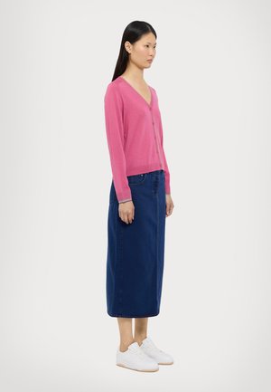 Cardigã tricotado rosa com decote em V e botões, combinado com uma saia de ganga azul e ténis brancos. Textura suave e design casual.