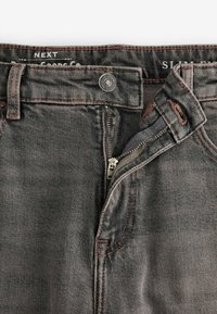 Jeans slim-fit din denim gri închis, cu cusături portocalii contrastante. Dispune de un nasture metalic, fermoar și bucle pentru curea.