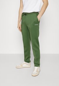 Groene sweatpants met een trekkoord in de taille en zijzakken, met een wit "LES DEUX" logo op de linker dij. Glad stofoppervlak.