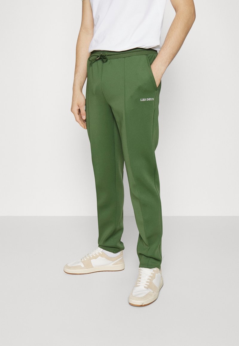 Groene sweatpants met een trekkoord in de taille en zijzakken, met een wit "LES DEUX" logo op de linker dij. Glad stofoppervlak.