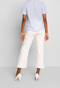 Ljusblå, randig kortärmad topp med ett sprund bak, kombinerad med krämfärgade vida byxor och vita högklackade skor.