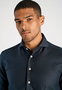 Donkerblauw overhemd met knopen, gemaakt van glad weefsel, met een puntige kraag en witte knopen aan de voorkant, dat een getailleerde silhouet biedt.