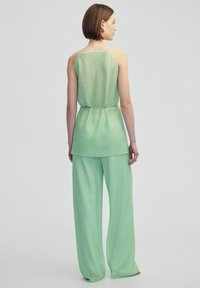 Completo due pezzi verde menta composto da un top senza maniche con texture e pantaloni a gamba larga. Il tessuto è leggero e semi-trasparente.
