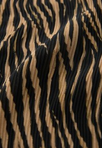 Tissu texturé présentant un motif ondulé en noir et en beige, avec des ondulations prononcées et des rayures alternées, créant un effet visuel dynamique.