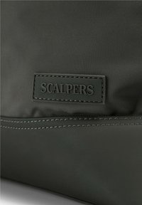 Bolsa de nylon negra con superficie texturizada, costuras en contraste y un parche de goma rectangular con el logotipo "SCALPERS" en relieve.