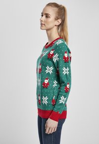 Zöld kötött pulóver, piros kiegészítőkkel, Mikulás mintákkal, fehér hópelyhekkel és texturált felülettel. Hosszú ujjakkal, bordázott mandzsettákkal.