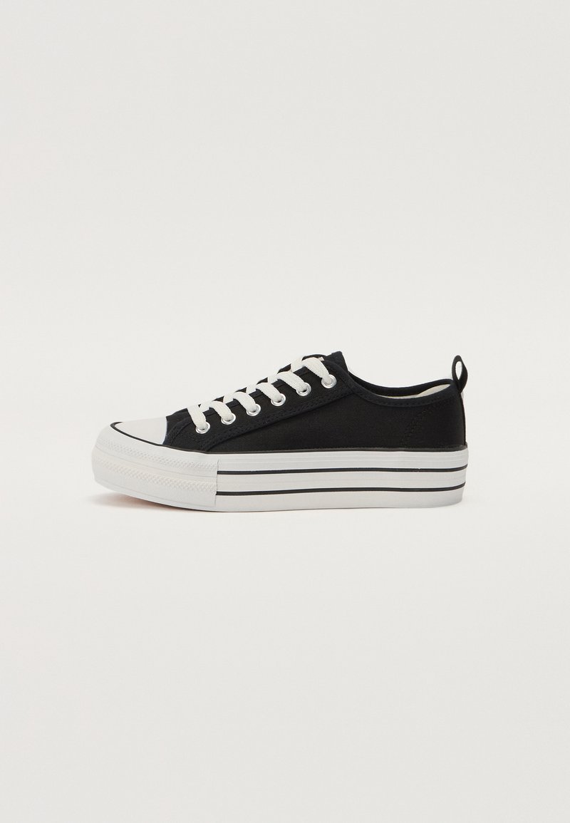 Sneaker nera in tela con punta arrotondata, suola in gomma bianca e tre strisce orizzontali bianche. Presenta lacci bianchi e un anello sul tallone.